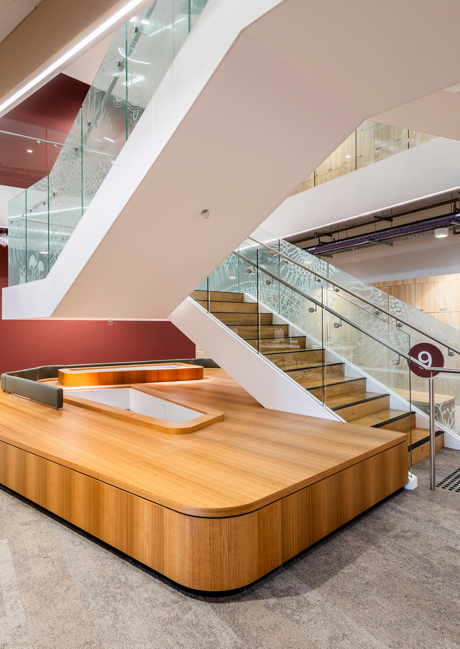 Atrium staircase with glazed balustrades and timber joinery rising through a double-height plasterboard void